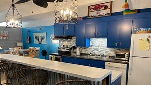 A modern kitchen with blue cabinets, a central island with bar stools, and a variety of appliances including a stove, oven, and microwave. - Huge Private Pool, Single Level Easy Access, 2 Golf Carts Included, Pet Friendly - 276 Tarpon Blvd (Fripp Island)