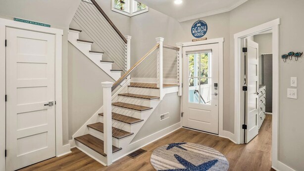 Una escalera con escalones de madera y paredes blancas, una puerta con un letrero, y una alfombra redonda con un diseño de flecha azul.