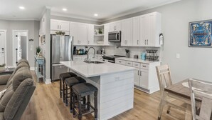 Una cocina moderna con armarios blancos, un refrigerador de acero inoxidable, horno empotrado y una isla grande con taburetes.