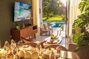 Un salon moderne doté d’un téléviseur, d’une table à manger et offrant une vue sur une piscine et un jardin.