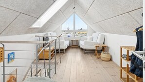 A loft bedroom with a sloped ceiling, a view of the city, a white sofa, a small table, and a wooden shelf. - "Pejo" - 10m from the sea by Interhome (Glesborg)