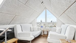 A modern loft bedroom with a sloped ceiling, two white sofas, a wooden TV stand, and a large window overlooking a marina. - "Pejo" - 10m from the sea by Interhome (Glesborg)
