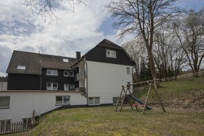 A two-story residential building with a black and white exterior, a visible balcony on the upper floor, and a wooden swing set in the yard. - Apartment - Winterbergerstrasse 3 nr 505 (Winterberg)