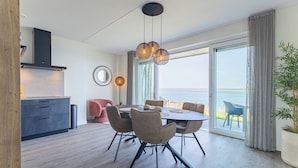 A modern dining area with a table and chairs, a pendant light, a view of the sea, and a large window.
