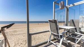 A beach view from a covered deck with a table and chairs, a hanging lantern, and a wooden walkway leading to the beach. - Slaapstrandhuisje - Strand Dishoek 37 I Dishoek (Koudekerke)