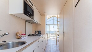 A narrow kitchen with a stainless steel sink, a stove, and cabinets. A ladder leads to a balcony with a view. - Slaapstrandhuisje - Strand Dishoek 37 I Dishoek (Koudekerke)