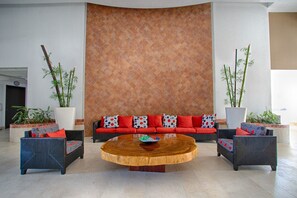 A lobby with a curved wooden coffee table, a red sofa with patterned cushions, and two potted plants. - Puerto Vallarta - Grand Venetian 9th Floor 1 Bedroom Beach Front & Water View (Puerto Vallarta)