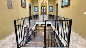 Una imponente escalera con barandales negros, un candelabro y cuadros enmarcados en las paredes.
