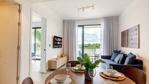 A dining area with a table set for four, a sofa, a TV, and a balcony with a view. - 1BR, artificial beach, pools, gym, location (Punta Cana)