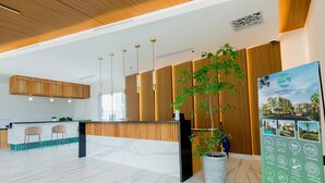 A modern reception area with a wooden reception desk, marble flooring, and a large potted plant. - 1BR, artificial beach, pools, gym, location (Punta Cana)