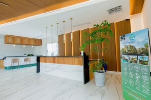 A modern reception area with a wooden reception desk, marble flooring, and a large potted plant. - 1BR, artificial beach, pools, gym, location (Punta Cana)