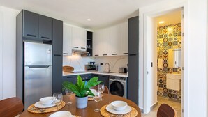 A dining area with a table set for four, a refrigerator, a washing machine, and a kitchen with white cabinets and a patterned backsplash. - 1BR, artificial beach, pools, gym, location (Punta Cana)
