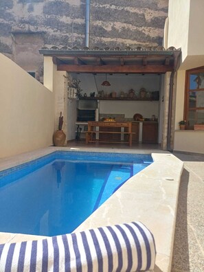 A swimming pool with a tiled edge, a wooden deck, and a kitchen area visible through an open doorway. - Alacantí House. Cozy house with pool and patio in Pollença (Pollença)