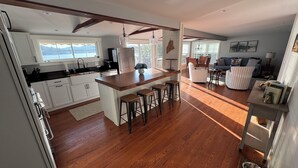 A modern kitchen with wooden flooring, a central island with stools, and a dining area with a view. - Golden View lake house on Crawford Pond (Union)