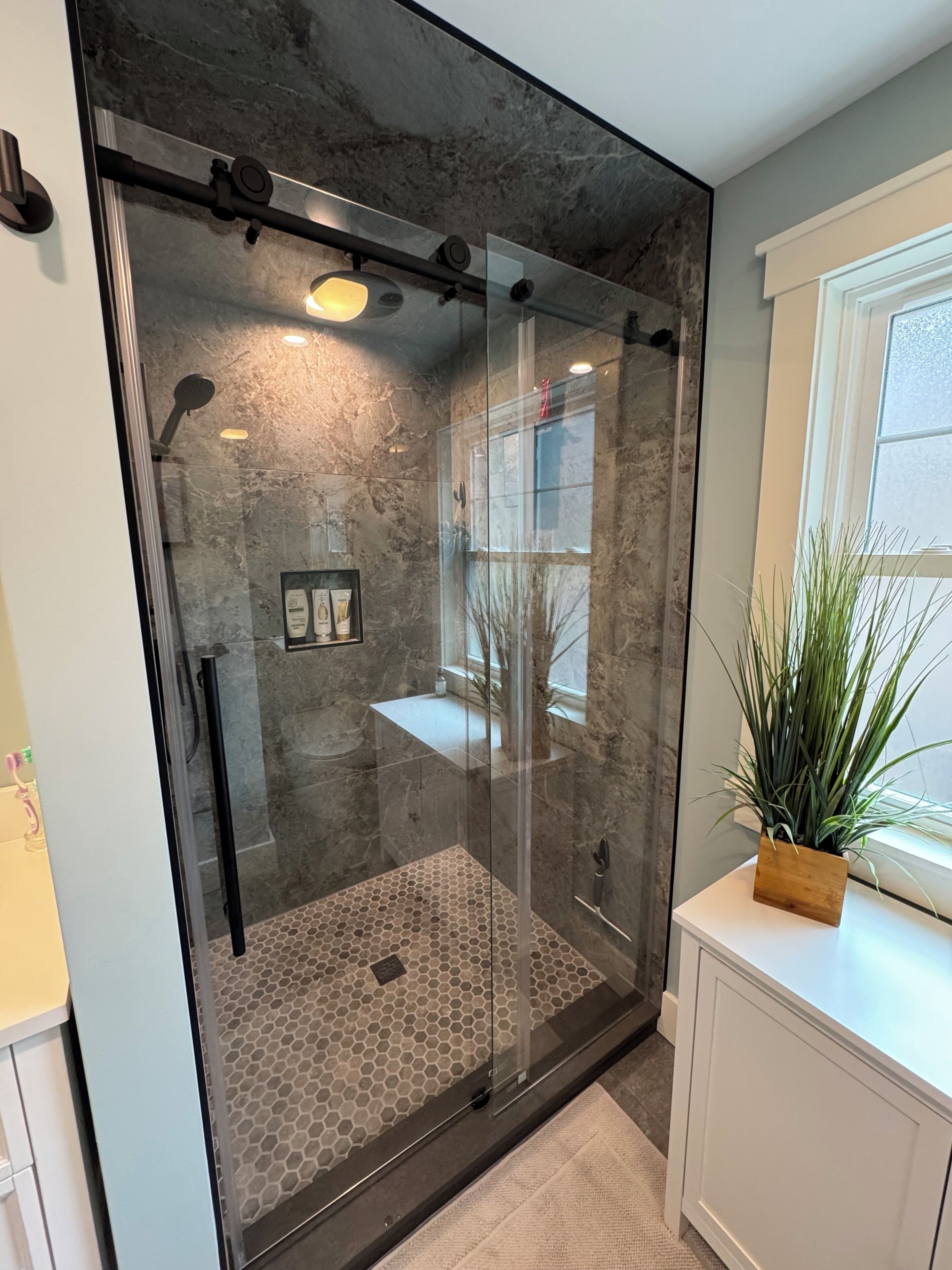 A modern shower with glass doors, a visible showerhead, and a small shelf with toiletries.