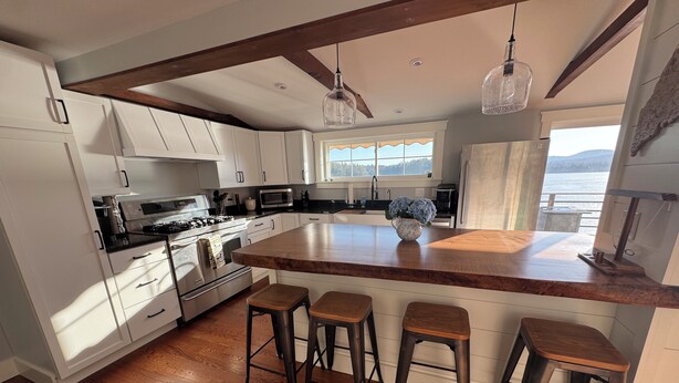 A kitchen with white cabinets, a wooden island with stools, a stove, and a view of the outdoors. - Golden View lake house on Crawford Pond (Union)