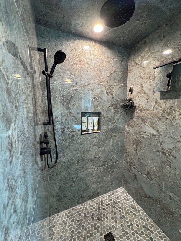 A modern bathroom with a shower, a mirror, and a small shelf with toiletries. - Golden View lake house on Crawford Pond (Union)