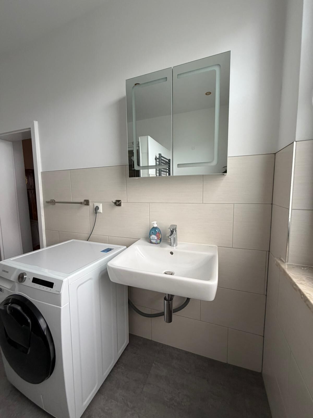 A compact laundry room with a washing machine, a sink, and a mirror.
