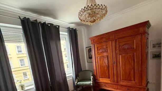 Une chambre avec deux lits, une armoire en bois, une chaise et un lustre.