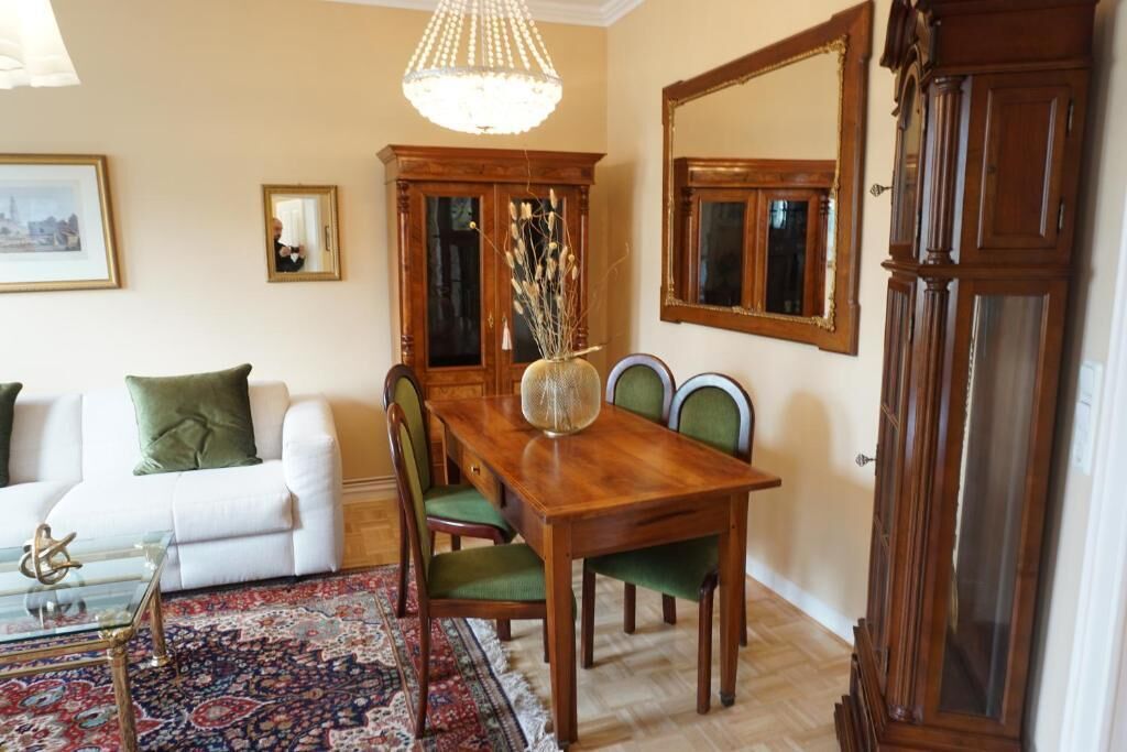 A dining area with a wooden table and chairs, a chandelier, a cabinet, and a mirror.
