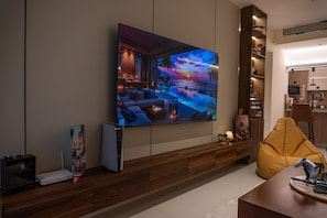 A modern living room with a large flat-screen TV, a wooden entertainment unit, a yellow bean bag, and a minimalist design. - Copper Living (Muscat)