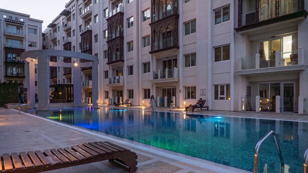 Une piscine avec des chaises longues, un chemin en pierre et un immeuble à plusieurs étages doté de balcons.
