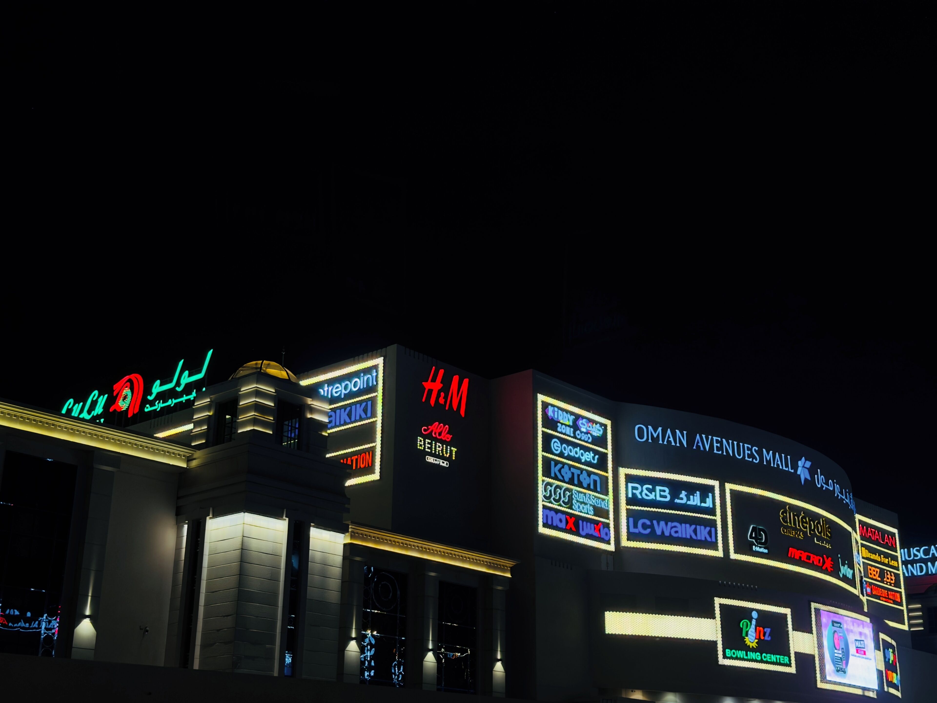 Un edificio con letreros iluminados de distintos negocios, entre ellos un centro de bolos y un centro comercial.