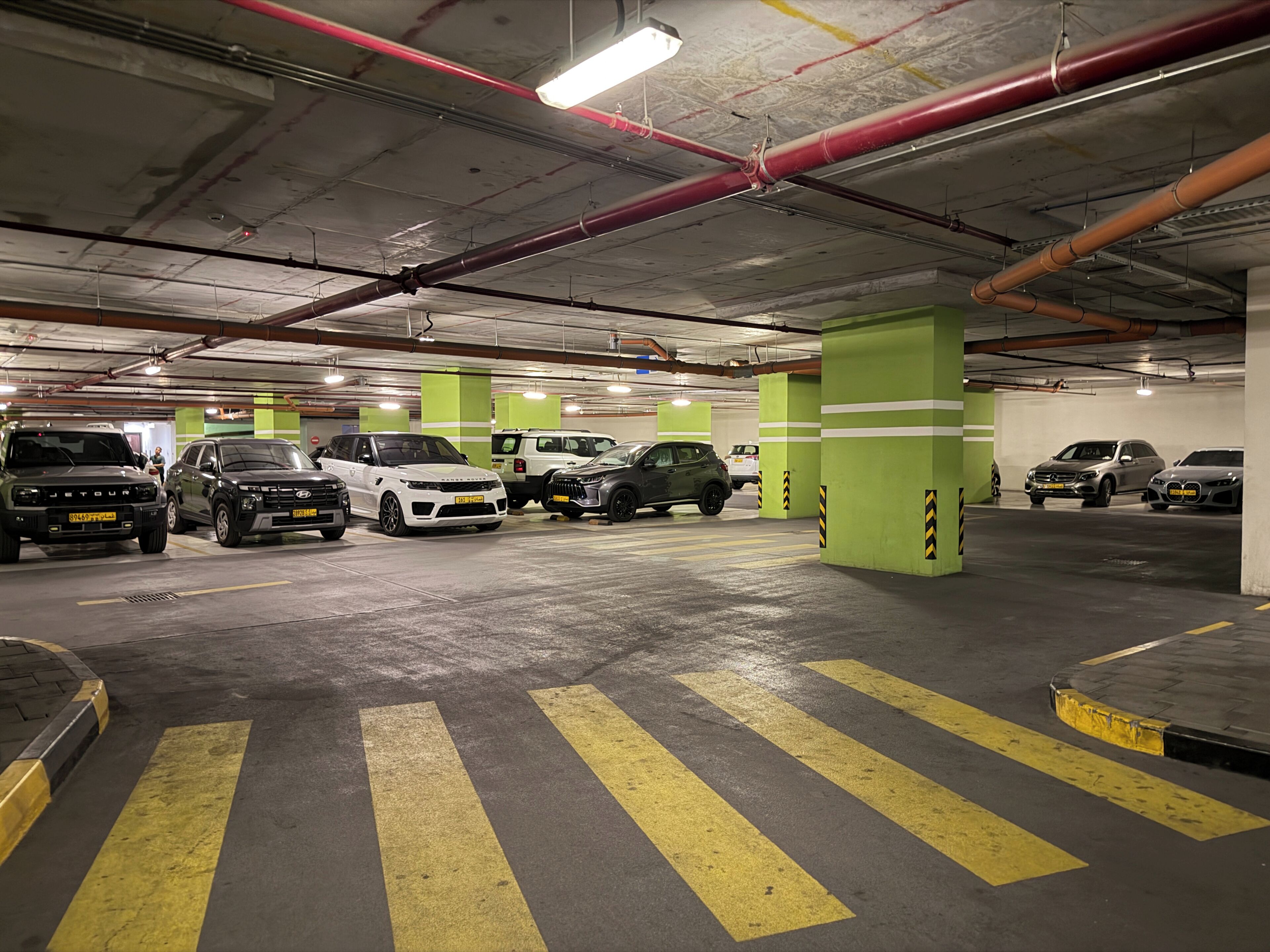 A multi-level underground parking garage with several cars parked, green pillars, and yellow parking lines.