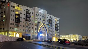 Un hôtel à plusieurs étages, doté d’une entrée monumentale en forme d’arc, de balcons et d’une enseigne lumineuse.