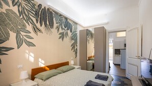 Quarto com cama, mesa de cabeceira e parede com padrão de folhas.