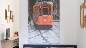 Quarto com cama, televisão presa à parede e quadro com imagem de um elétrico.