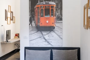 Una stanza con un letto, una TV a parete e un quadro con un tram.