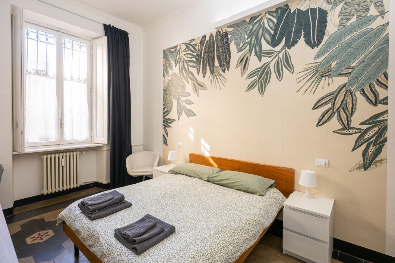 Une chambre à coucher comprenant un lit, une table de chevet, une chaise, une fenêtre avec des rideaux et un radiateur.