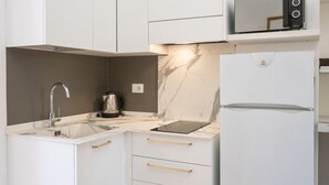Cozinha moderna com armários brancos, pia de aço inoxidável, chaleira preta, painel de apoio de mármore e micro-ondas embutido.
