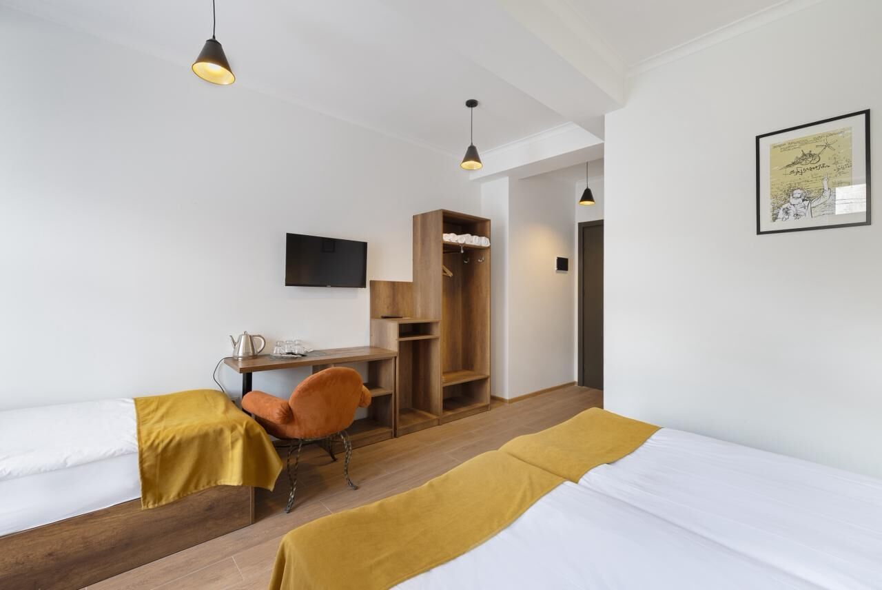 Een hotelkamer met twee eenpersoonsbedden, een bureau, een stoel, een televisie en een houten garderobe.