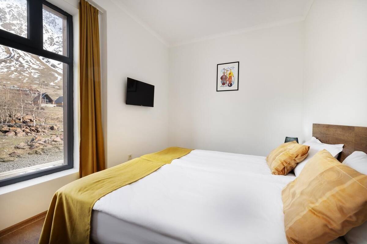 A hotel room with a bed, a window with curtains, a flat-screen TV, and a framed picture on the wall.