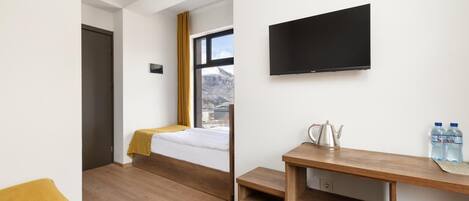 A room with a bed, a desk, a TV, and a window with a mountain view.