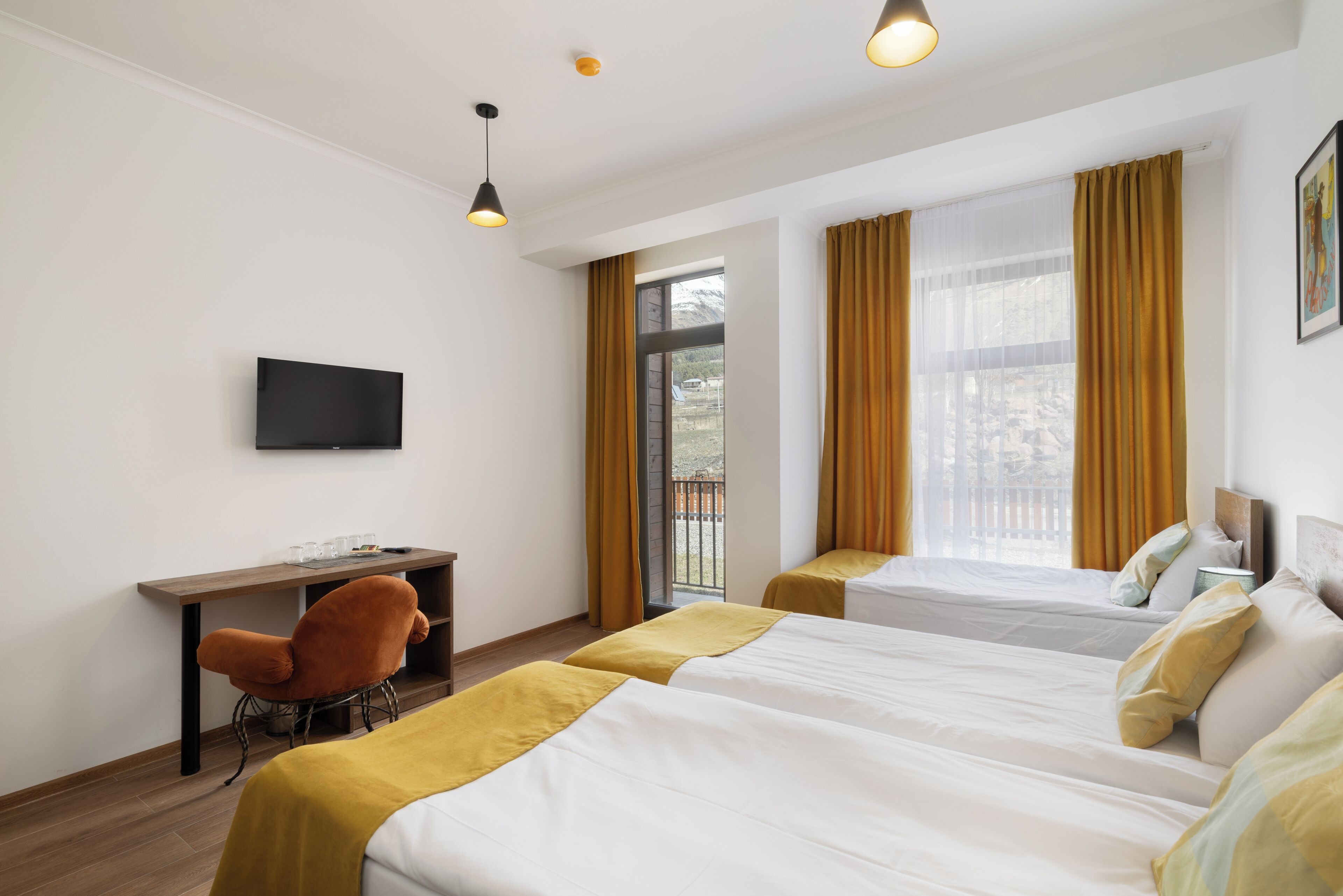 A hotel room with two beds, a desk, a chair, a TV, and large windows with curtains.