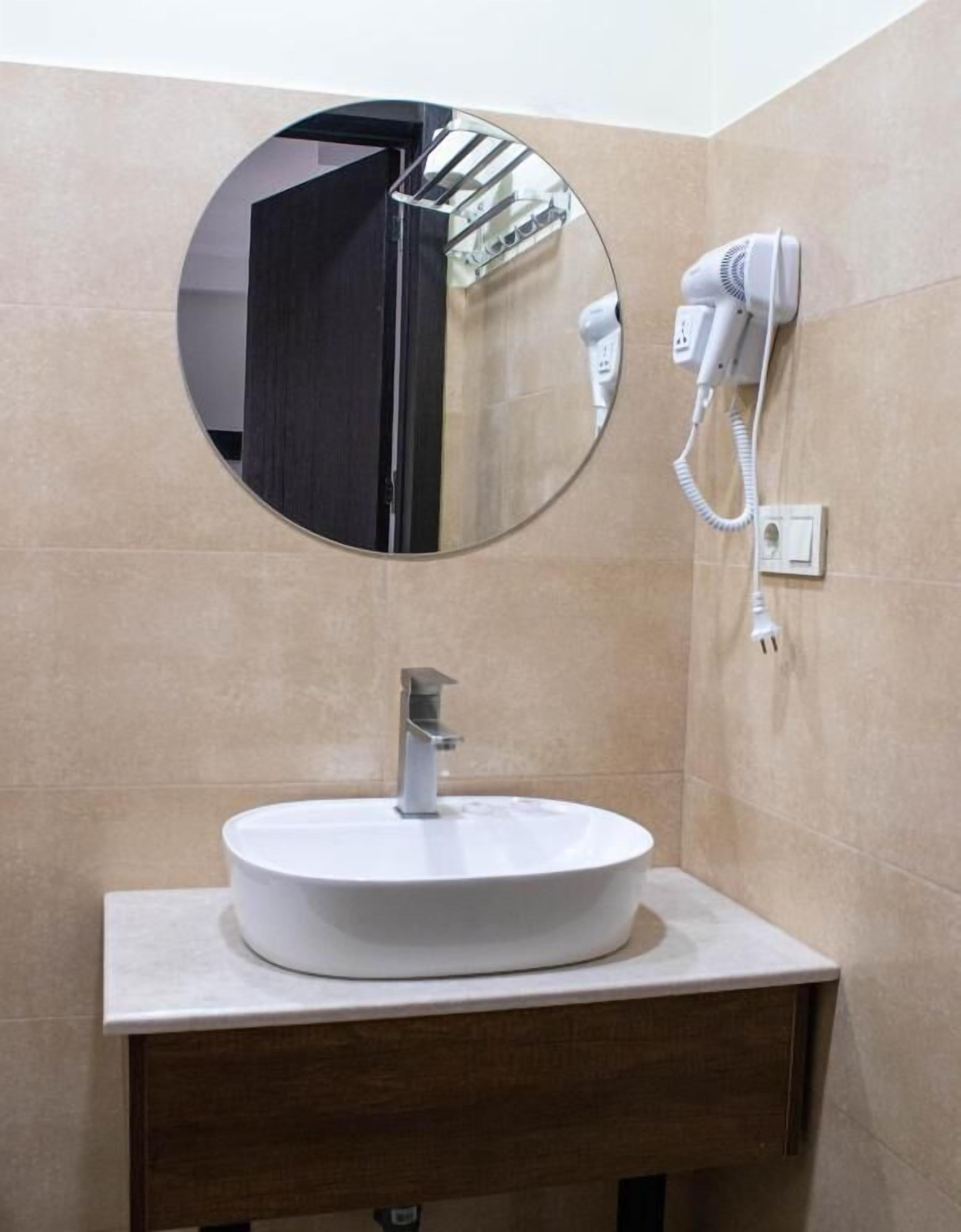 A bathroom with a round mirror, a white sink, and a hairdryer mounted on the wall.