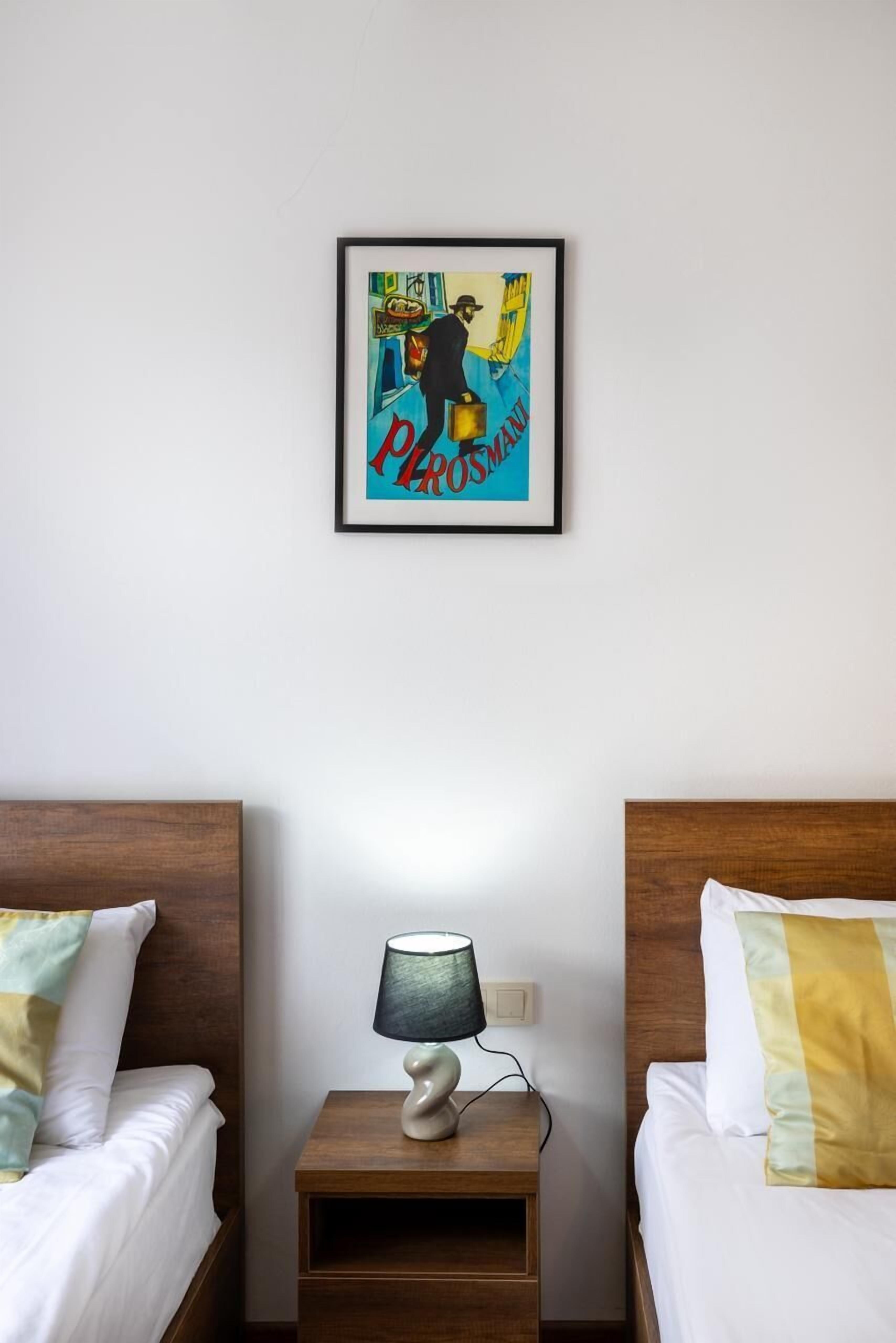 Una habitación de hotel con dos camas, una mesita de noche con una lámpara y un cuadro en la pared.