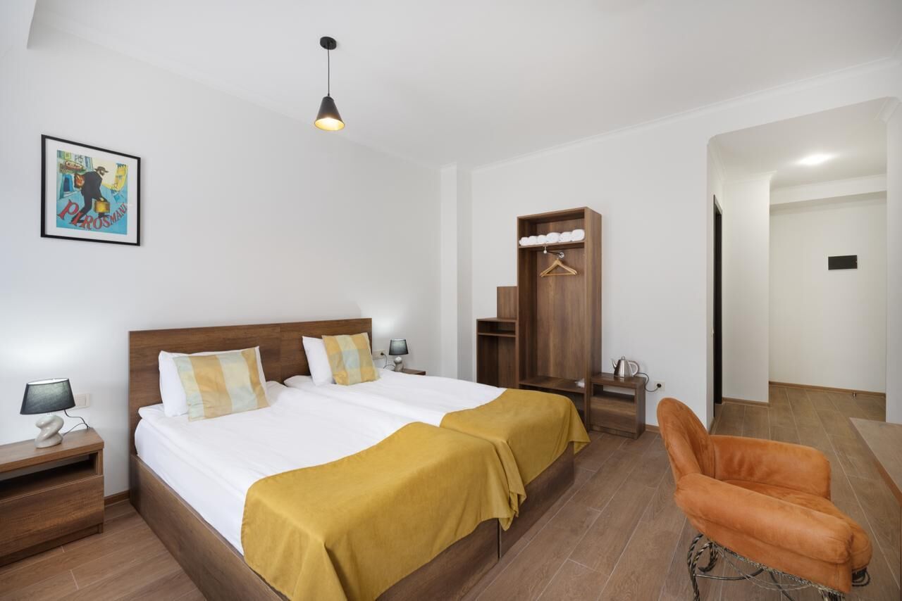 A hotel room with a double bed, a wooden wardrobe, a chair, and a framed picture on the wall.
