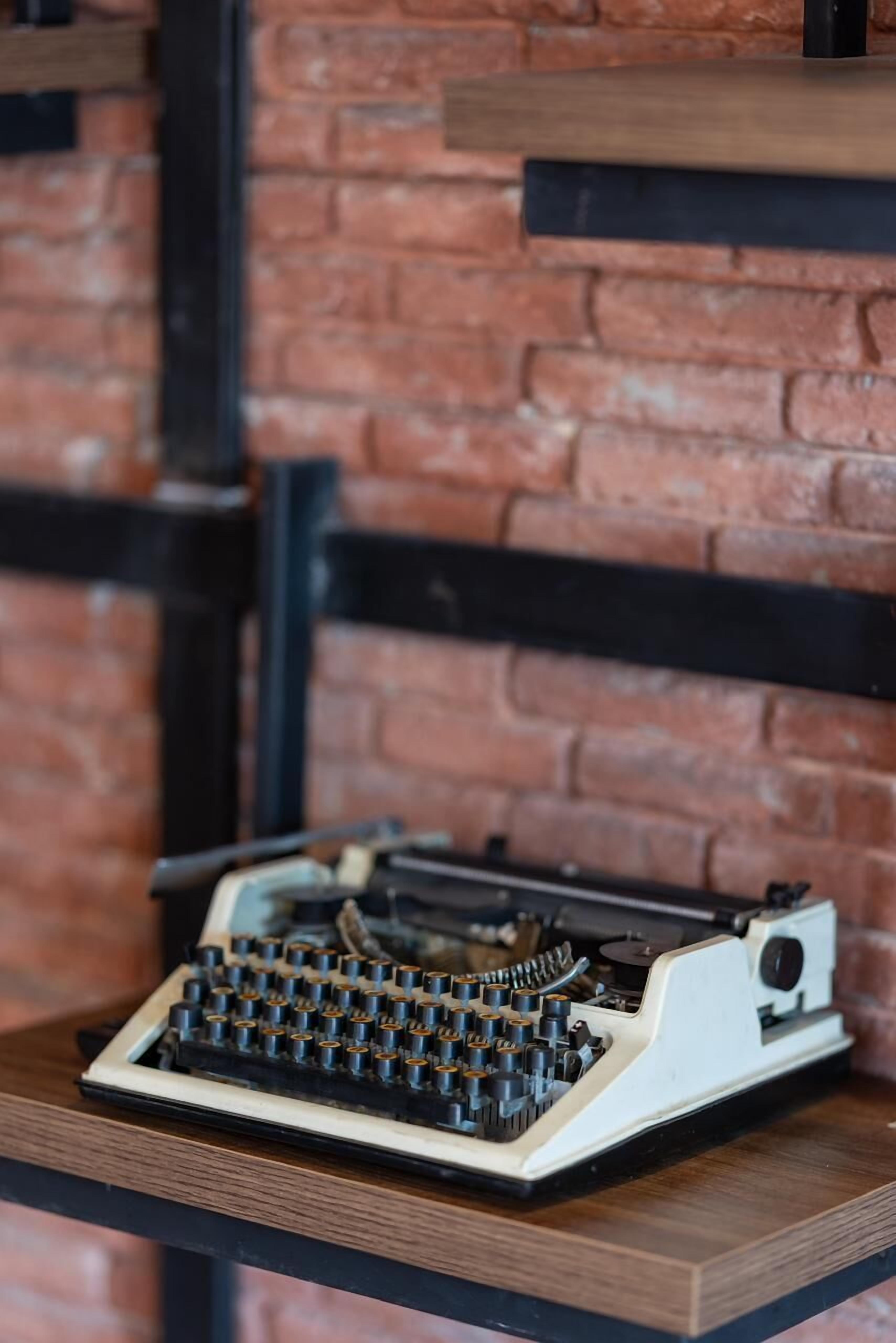 A vintage typewriter on a wooden table against a brick wall.