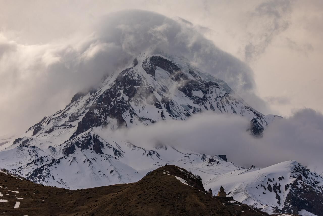 A snow-covered mountain with a rugged peak and a small building at its base.