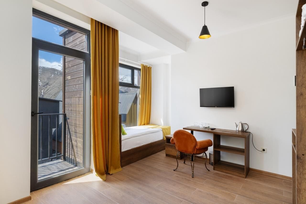Une chambre à coucher comprenant un lit, un bureau, une chaise, un téléviseur et un balcon avec des rideaux.