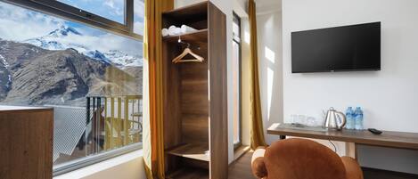 Una habitación moderna con un armario de madera, un televisor en la pared, un escritorio con una silla y vistas a montañas nevadas.