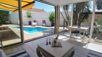 Une terrasse avec une piscine, du mobilier d’extérieur et une table sur laquelle se trouvent une bouteille et des verres.