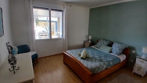 Un dormitorio con cama, mesitas de noche, un escritorio y una ventana.