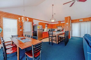A compact kitchen with wooden cabinets, a refrigerator, and a dining area with a table and chairs. - JL #656 | Terrill Cottage | Semi-Oceanfront | Horizon Ocean View (Kitty Hawk)