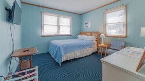 Ein Schlafzimmer mit einem Bett, zwei Fenstern, einem Schreibtisch und einem Sessel.