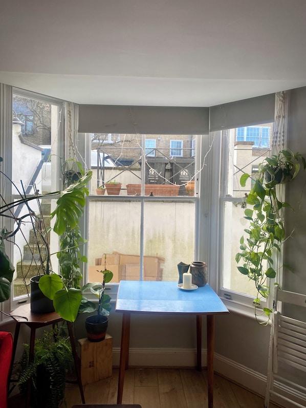 Une pièce d’angle avec une baie vitrée, une table avec une bougie et des plantes en pot.